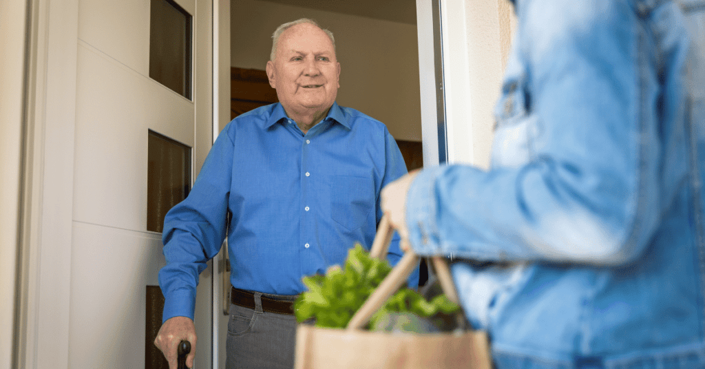 elderly caregiver dropping off groceries to elderly man at front door