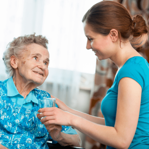 senior caregiver offering glass of water to elderly woman