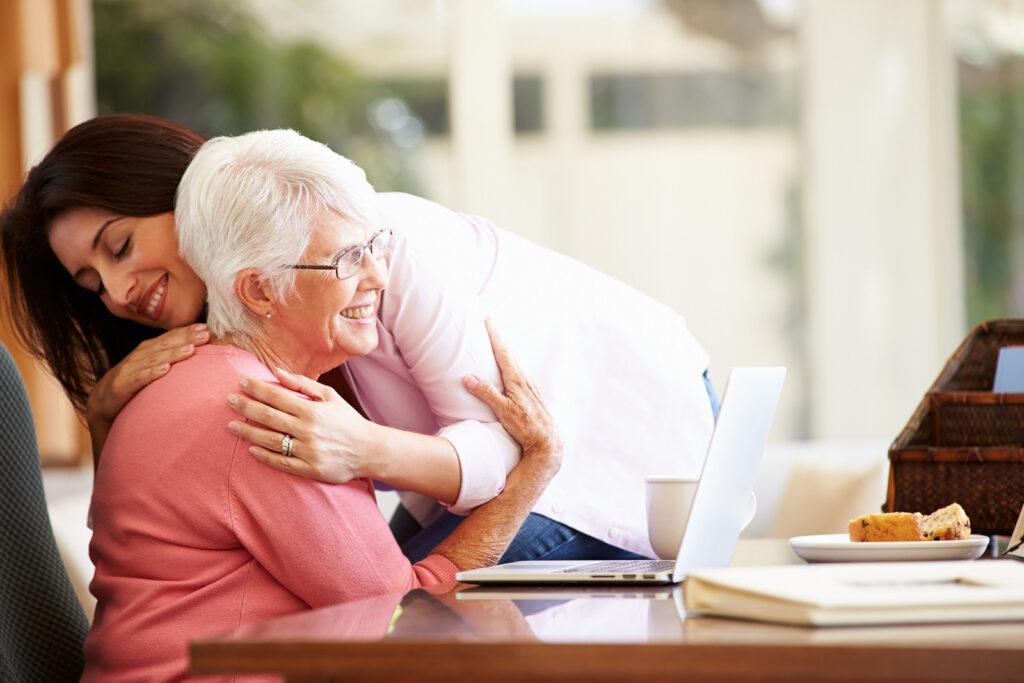 elderly care provider giving warm hug to elderly woman at table