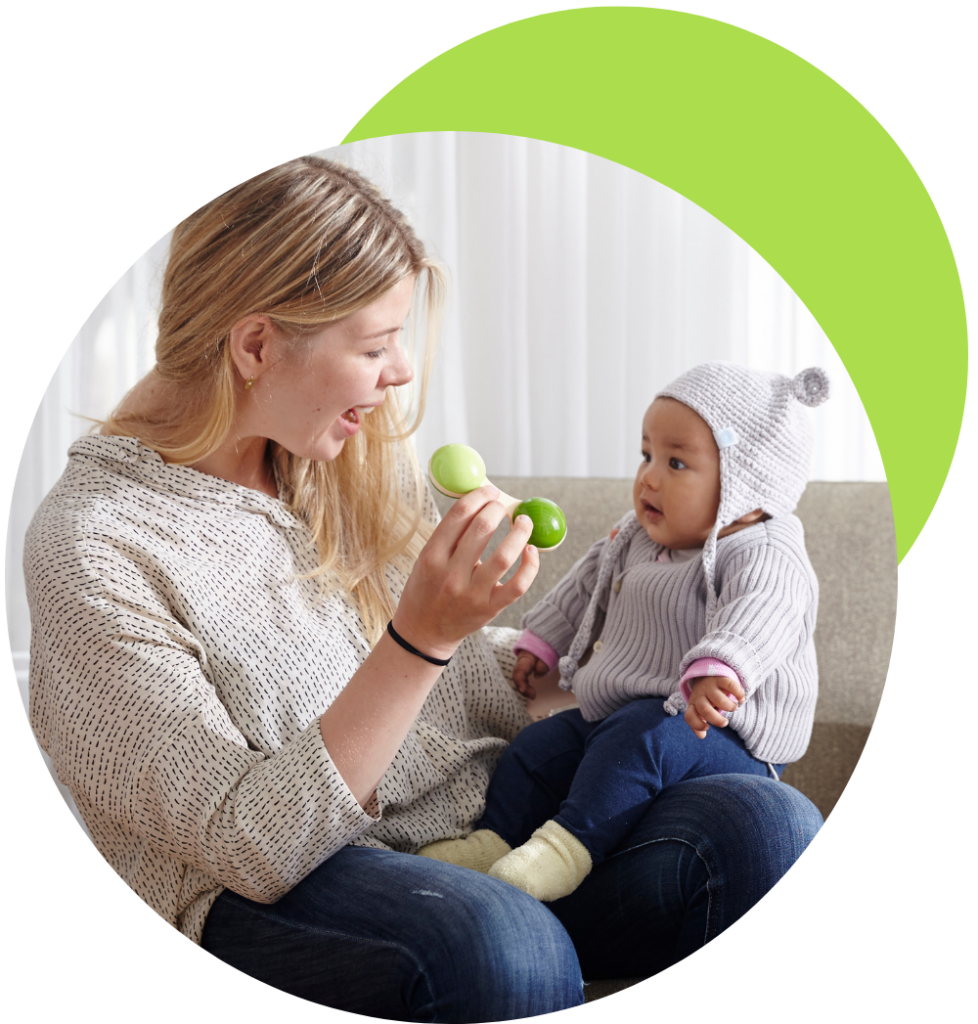 nanny shaking a rattle for an infant sitting on her lap