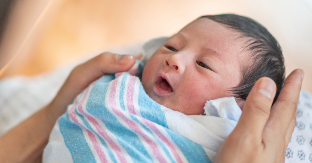 infant caregiver holding swaddled newborn baby